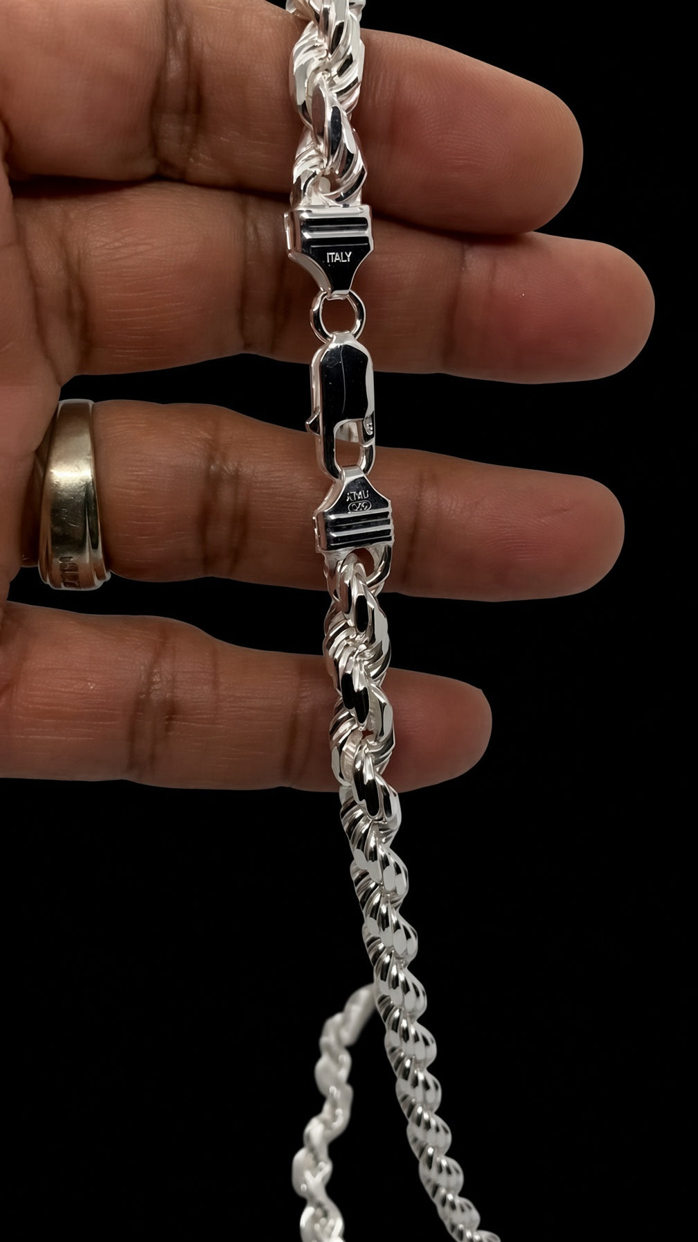 A close-up of a silver Cuban link chain bracelet being held by a hand against a solid black background. The clasp is engraved with the brand name 'PULSAR'.